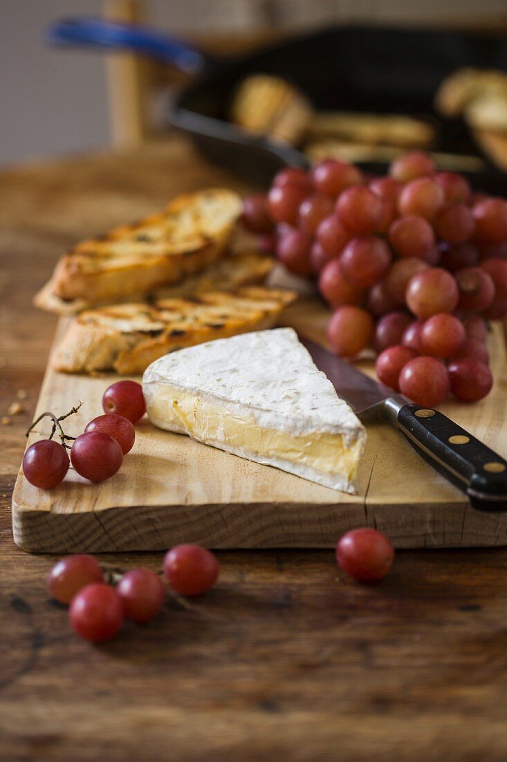 Brie, red grapes and grilled bread on a chopping board