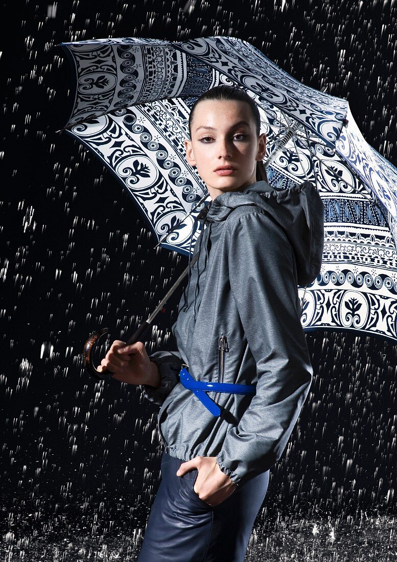 Junge Frau in blaugrauer Jacke unter farblich passendem Regenschirm