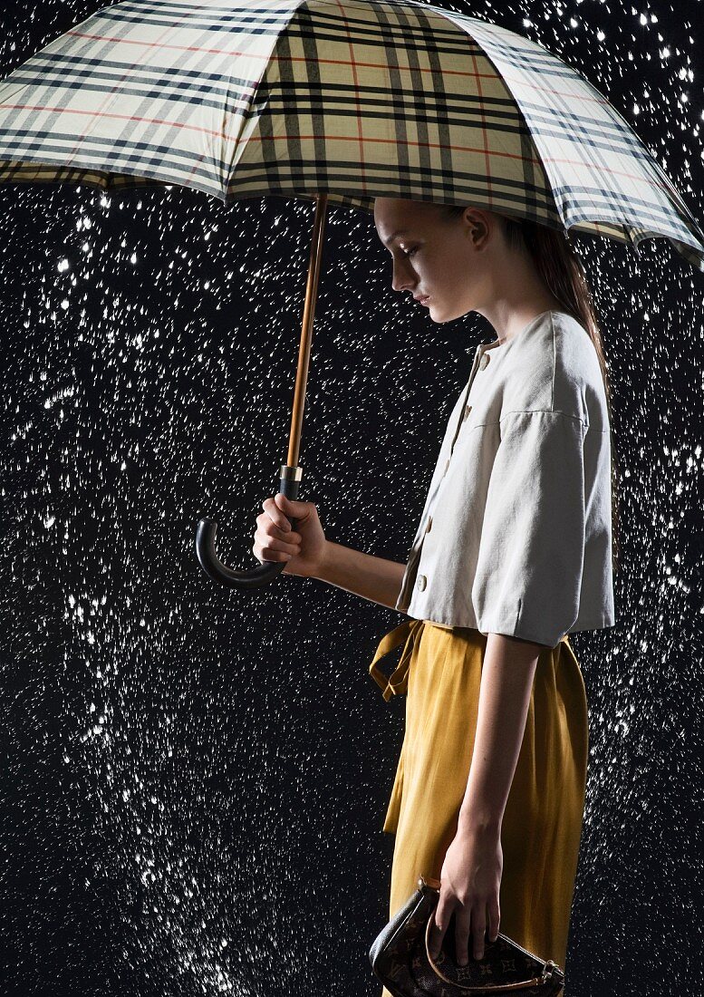 Junge Frau in weisser Bluse und gelbem Rock unter schwarz-gelb kariertem Regenschirm