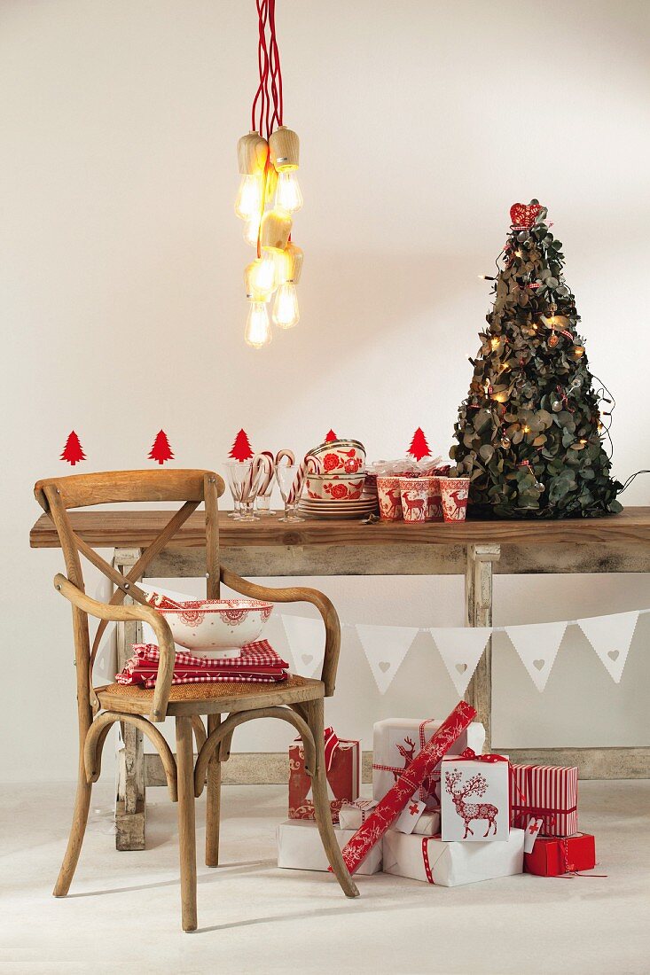 Pendant lamp above festively decorated rustic wooden ceiling, vintage chair and Christmas presents wrapped in red and white paper