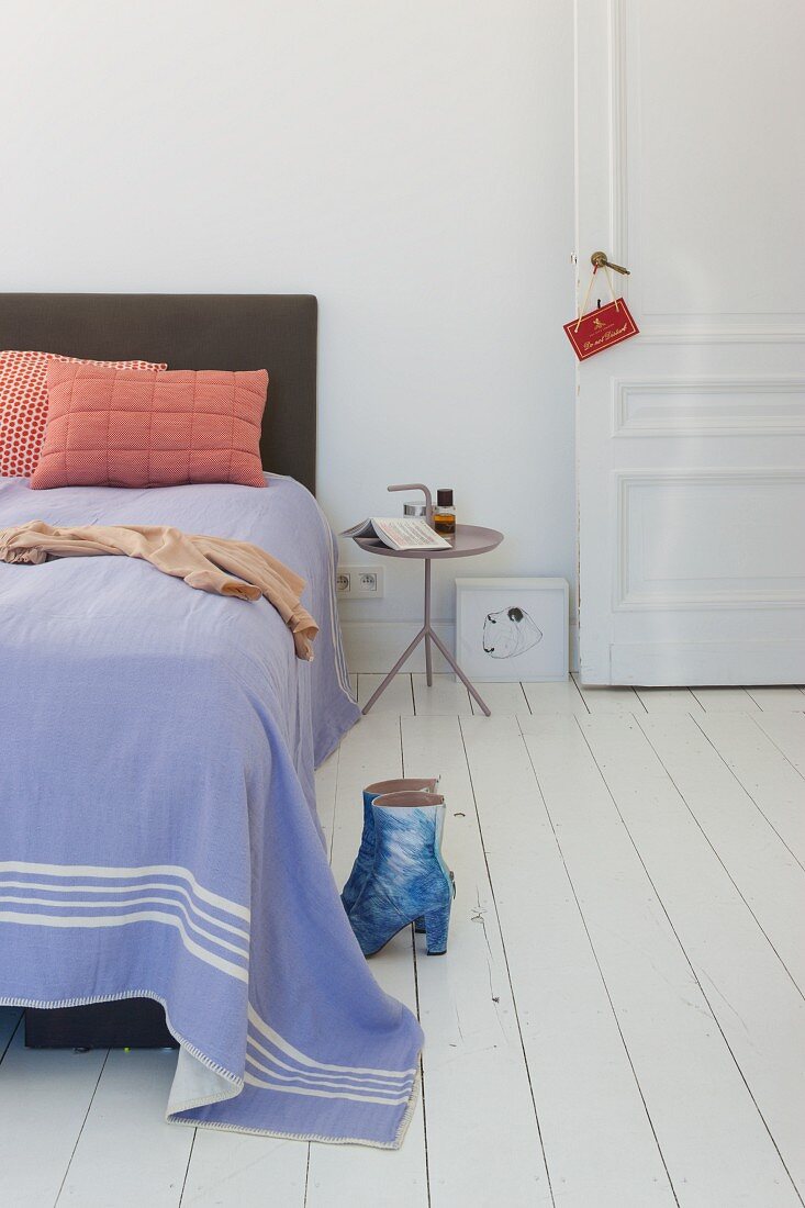 Bed with purple bedspread and boots on white wooden floor in period apartment