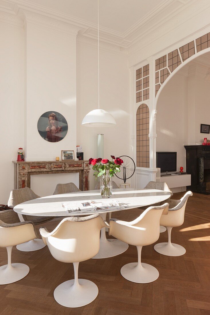 Tulip armchairs around vase of roses on oval table in front of traditional arched doorway with lead glazing