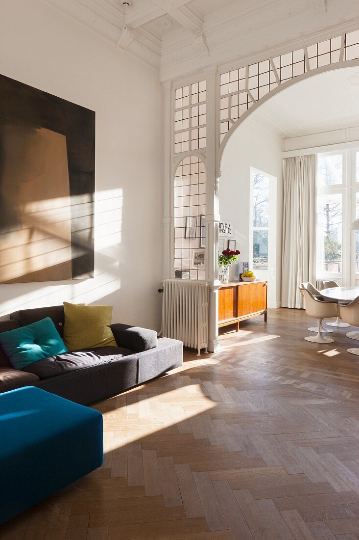 Wohnzimmerecke mit modernem Sofa vor Rundbogen mit Bleiverglasung und Blick in Essbereich