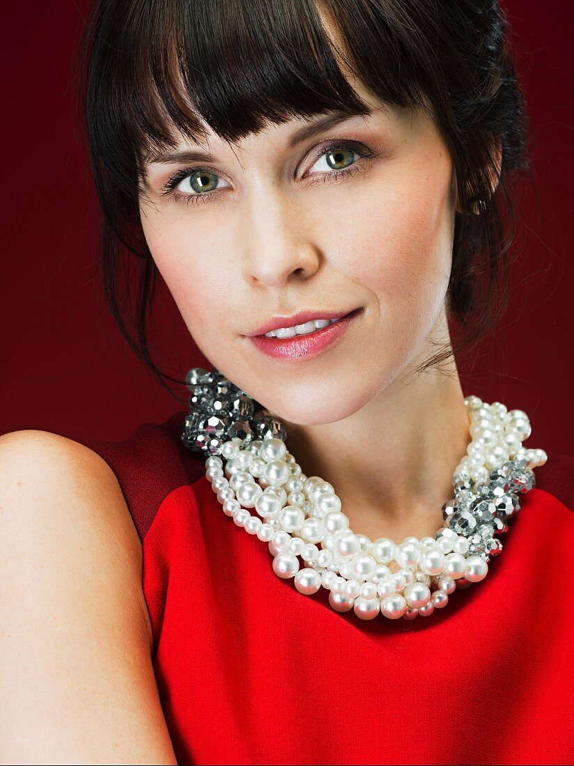 Dark-haired woman wearing red sleeveless dress and pearl necklace