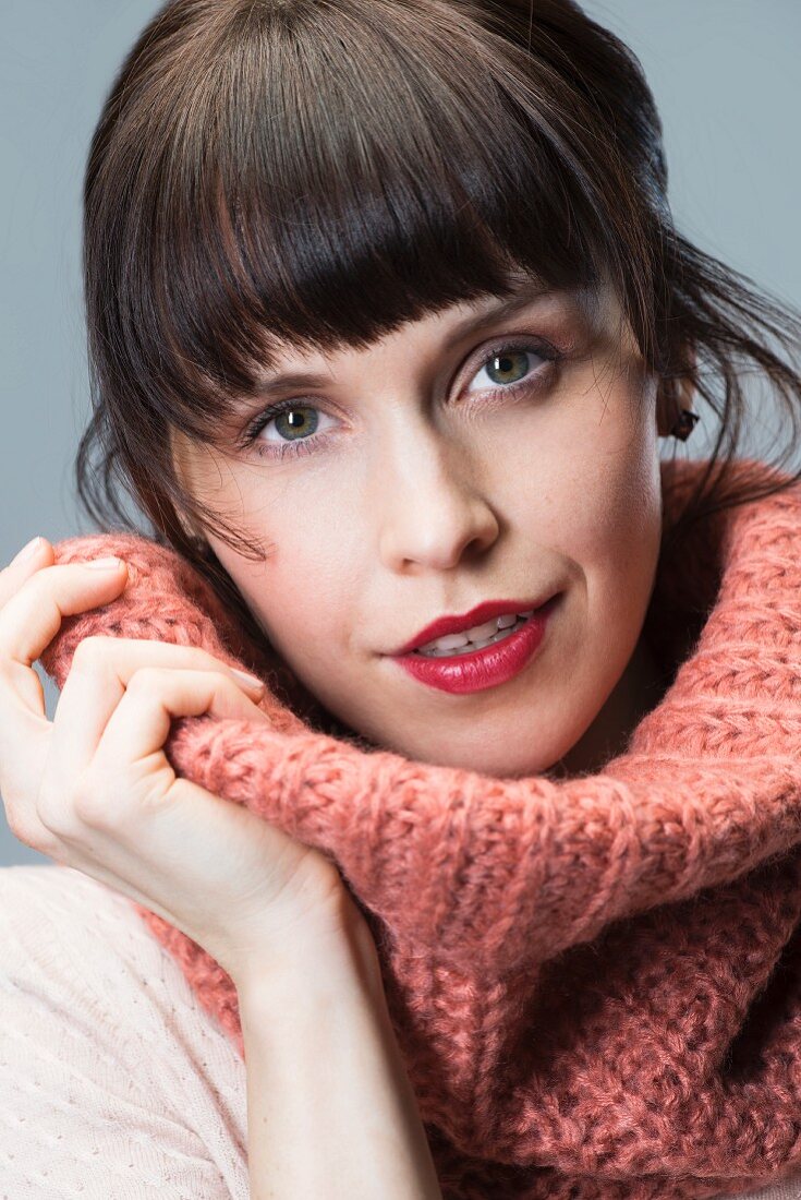 Dark-haired woman wearing salmon pink loop scarf