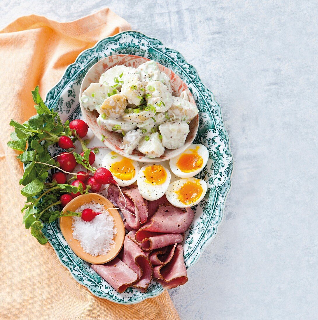 A cold platter with pastrami, hard-boiled eggs, potato salad and radishes