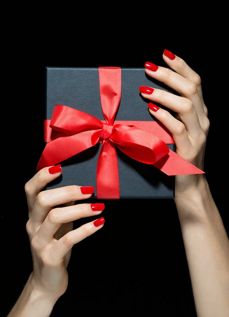 Frauenhände mit rot lackierten Fingernägeln halten Geschenkbox