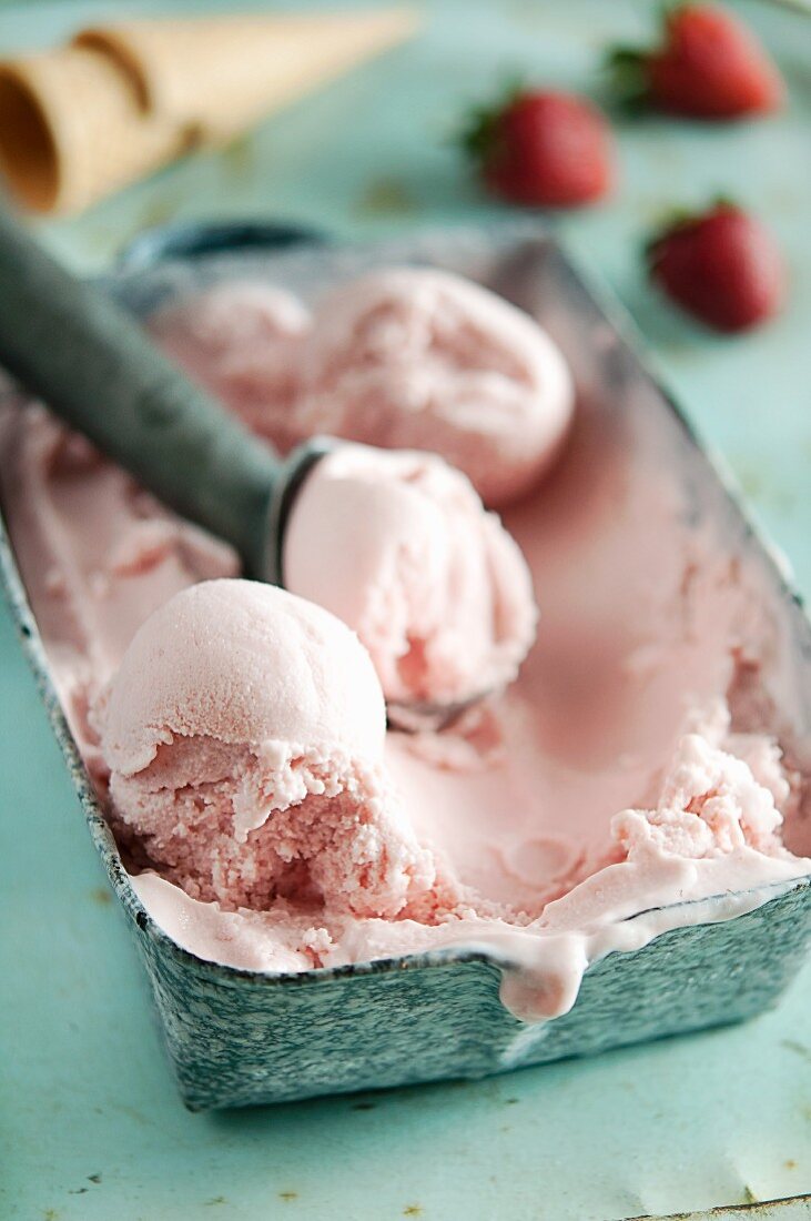 Strawberry yoghurt ice cream in an ice cream container with an ice cream scoop