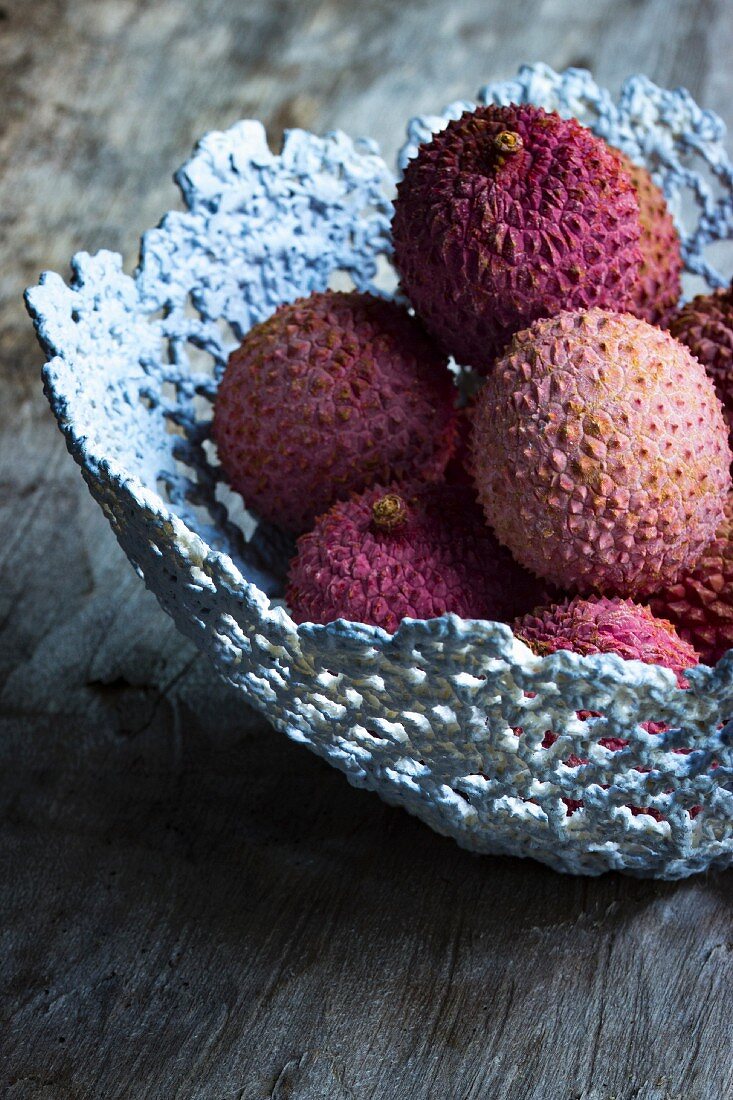 Lychees in a grey handmade basket on a wooden surface