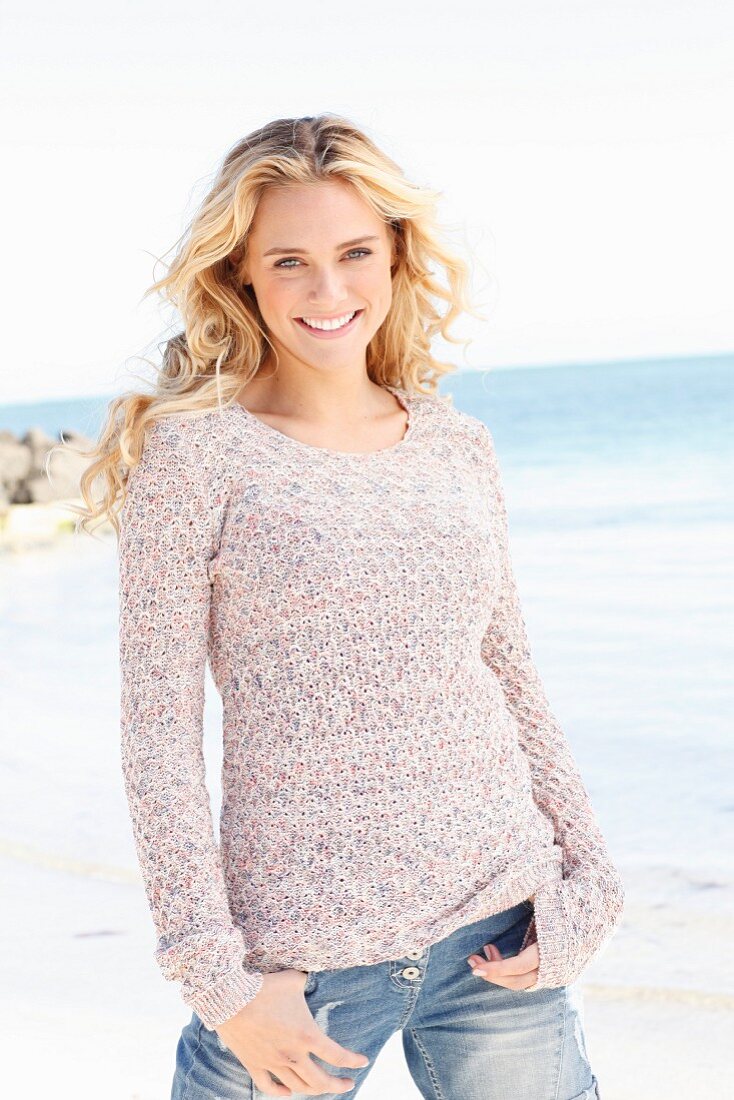 Junge blonde Frau in gestricktem Pulli und Jeans am Meer