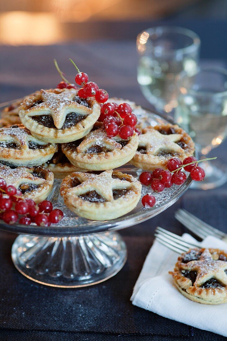 Hausgemachte Mince Pies mit Teigstern und Puderzucker auf Kuchenständer mit Johannisbeeren