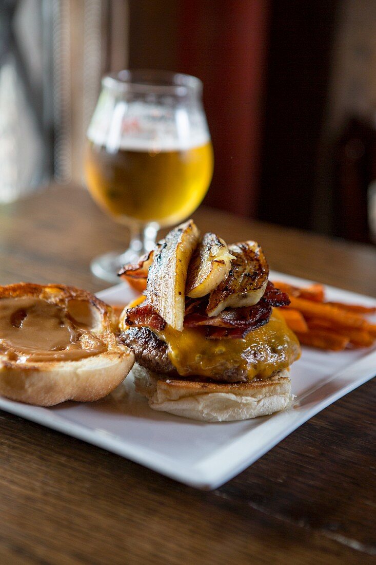 Cheeseburger with bacon and grilled bananas served with sweet potato fries and a glass of beer