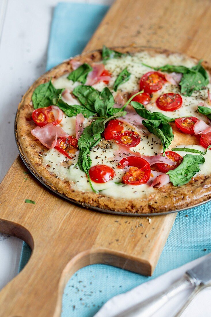 A pizza with ham, spinach and tomatoes
