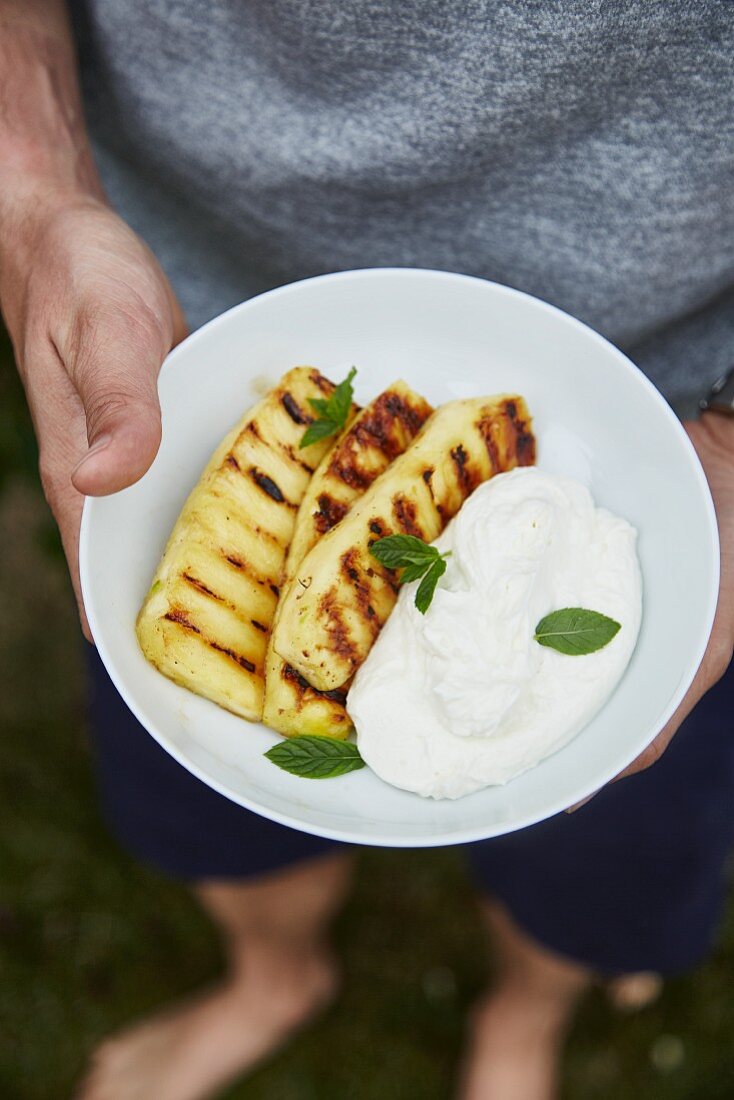 A man holding a plate of grilled pineapple and quark cream