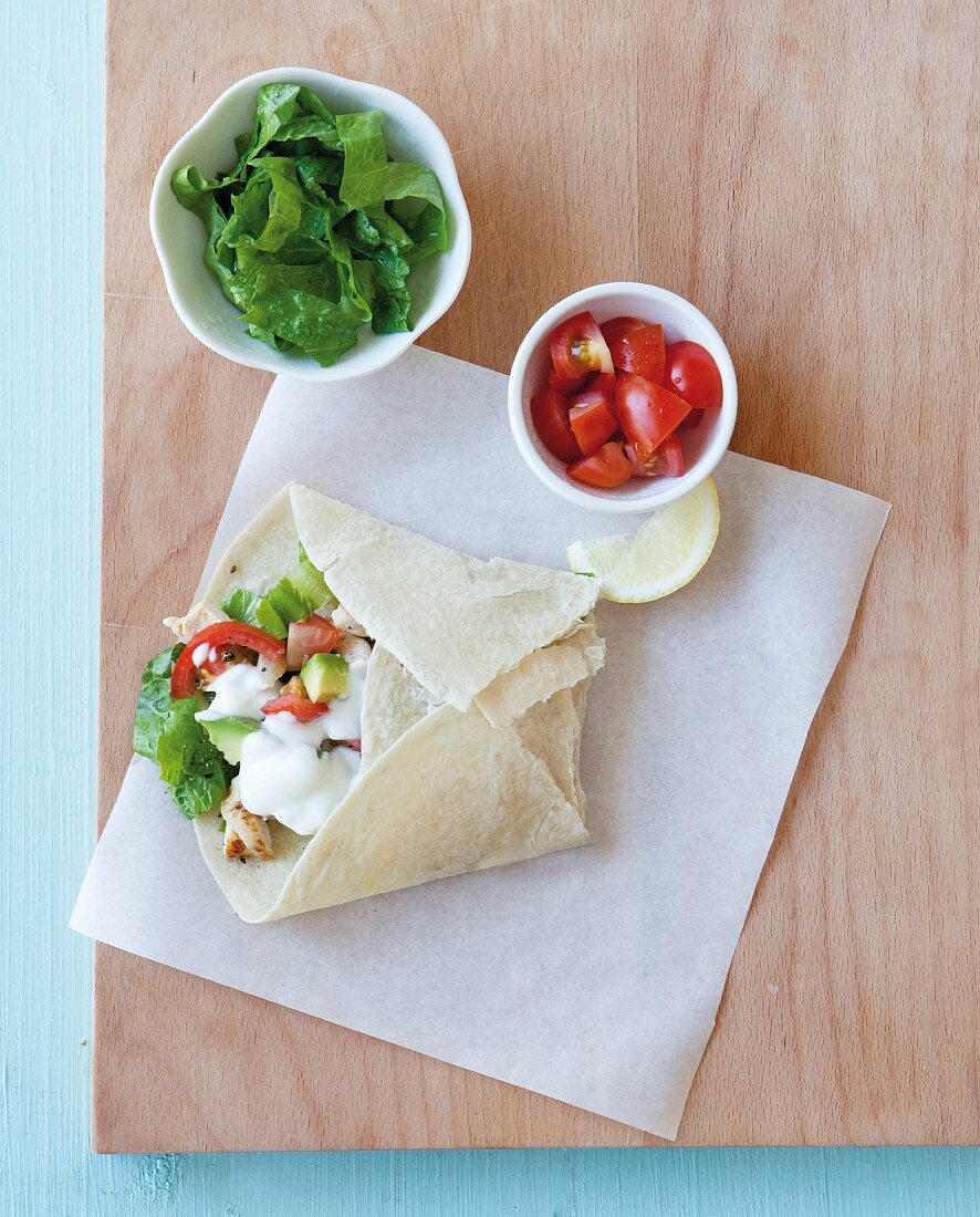 A burrito with avocado, tomatoes, lettuce and sour cream