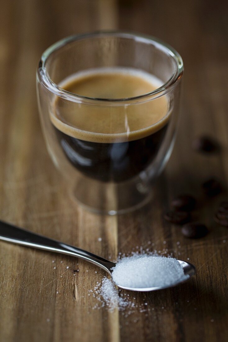Ein Espresso im Glas davor Kaffeelöffel mit Zucker