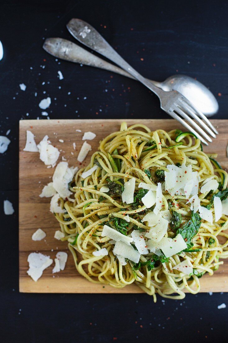 Pasta with courgettes, spinach and Parmesan cheese on a wooden board (seen from above)