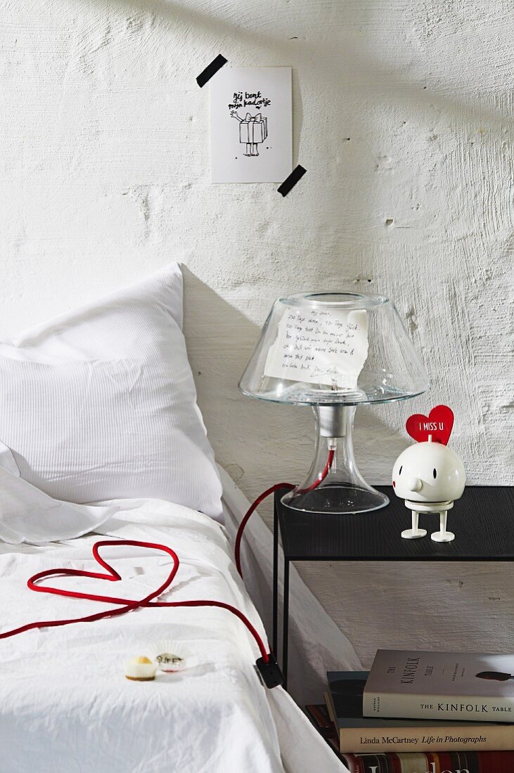 Bedroom decorated with love letter under clear lampshade and lamp power cable arranged as love-heart on bed