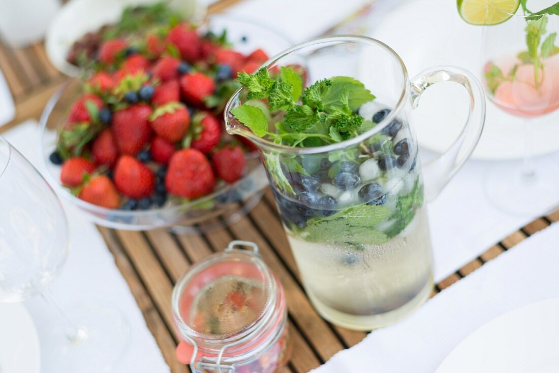 Refreshing drink with herbs in glass jug and glass dish of fresh berries
