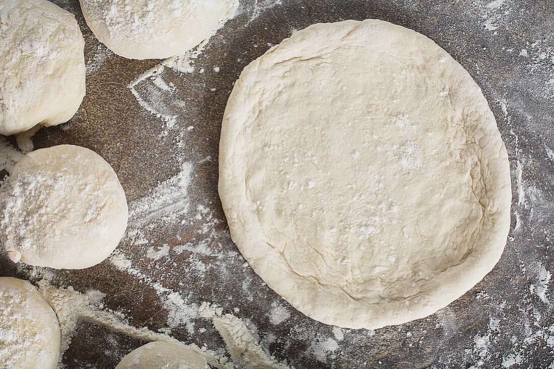 Boards of pizza dough and one rolled out
