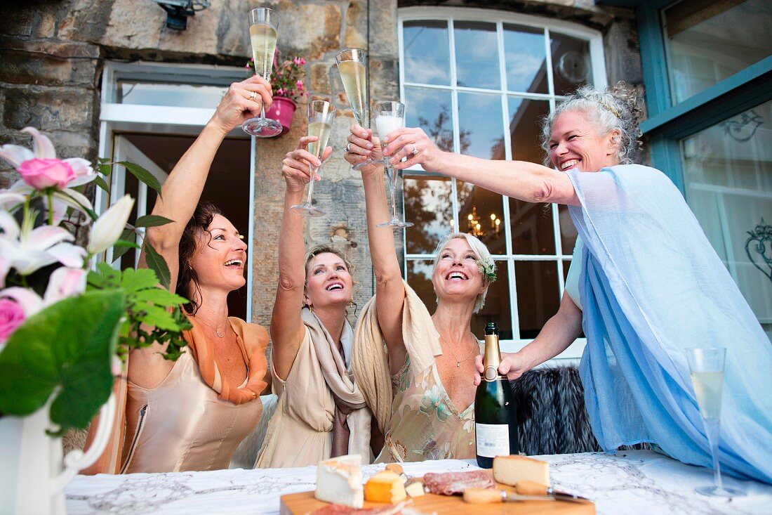 Four women wearing evening dresses toasting with champagne