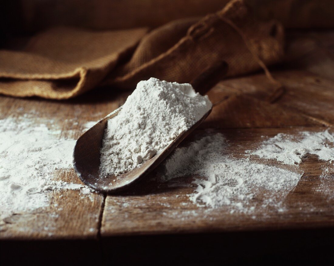 Wheat flour in a wooden scoop on an old wooden table