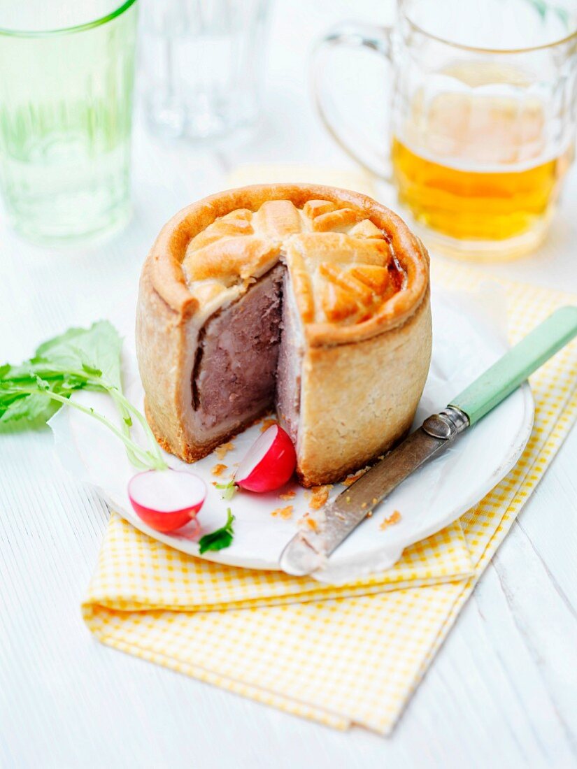 A sliced pork pie with radishes and beer