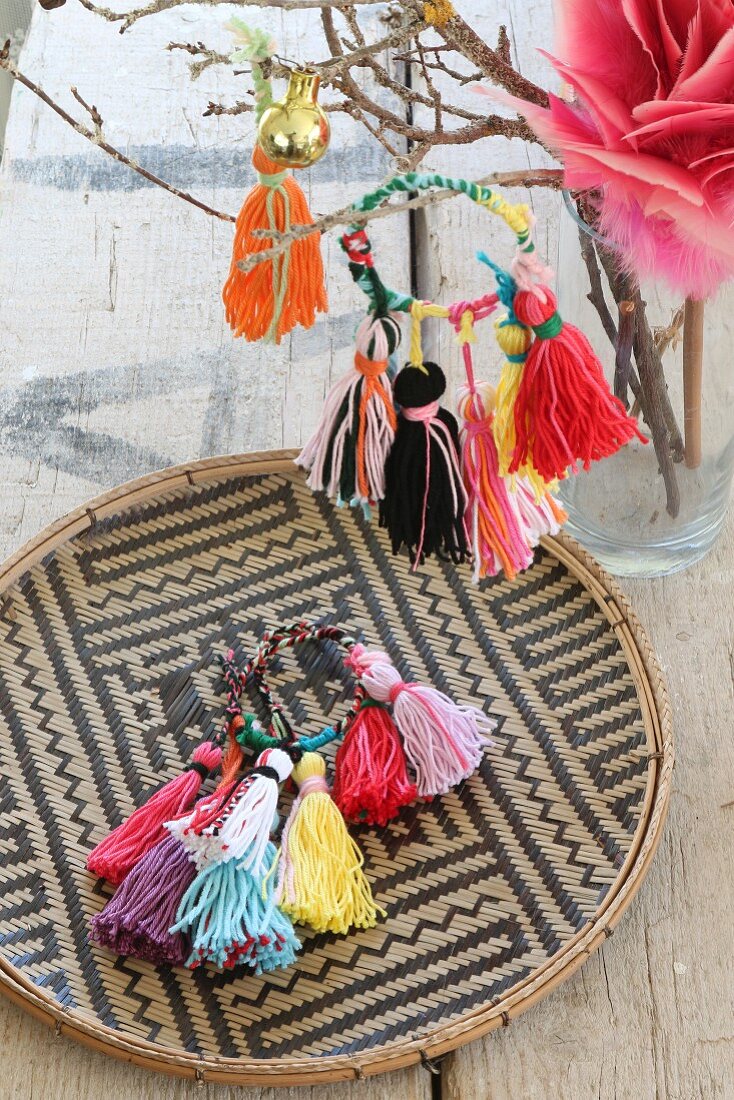 Colourful handmade woollen tassels on a raffia plate and hanging on a twig