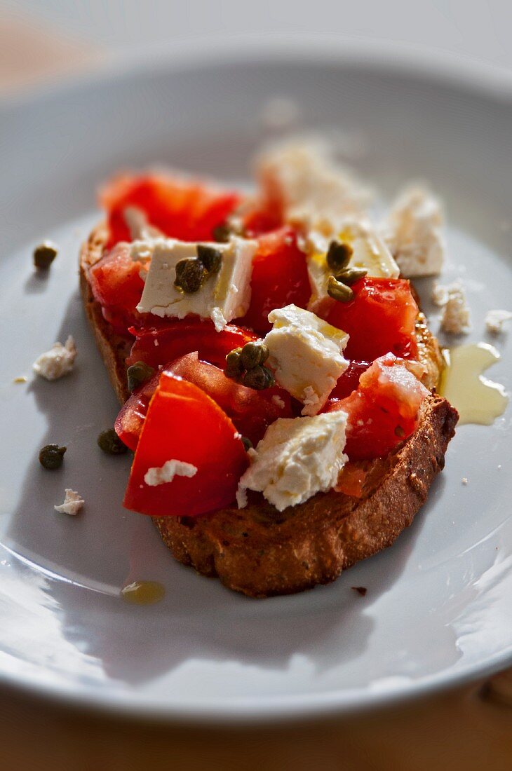 A slice of bread topped with tomatoes, feta cheese and capers