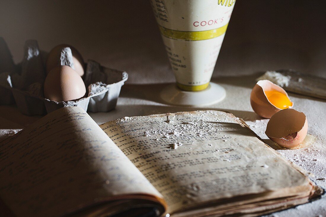 A baking scene with and old recipe book, eggs and flour