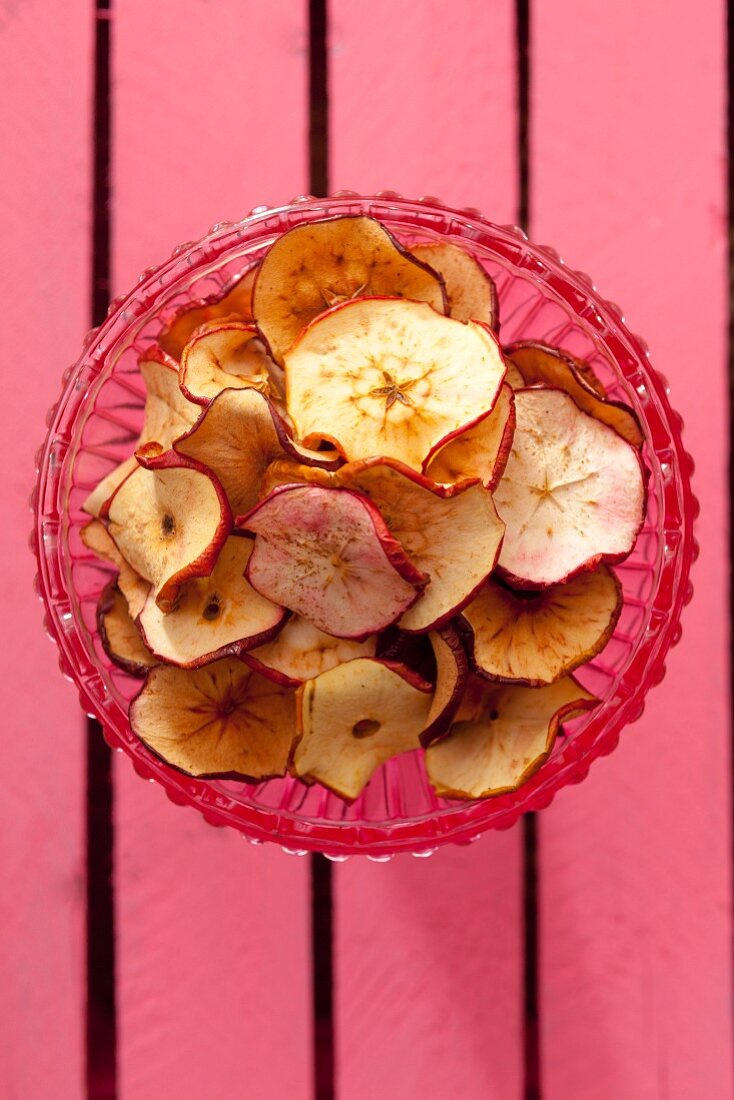 Homemade apple chips in a glass bowl (seen from above)