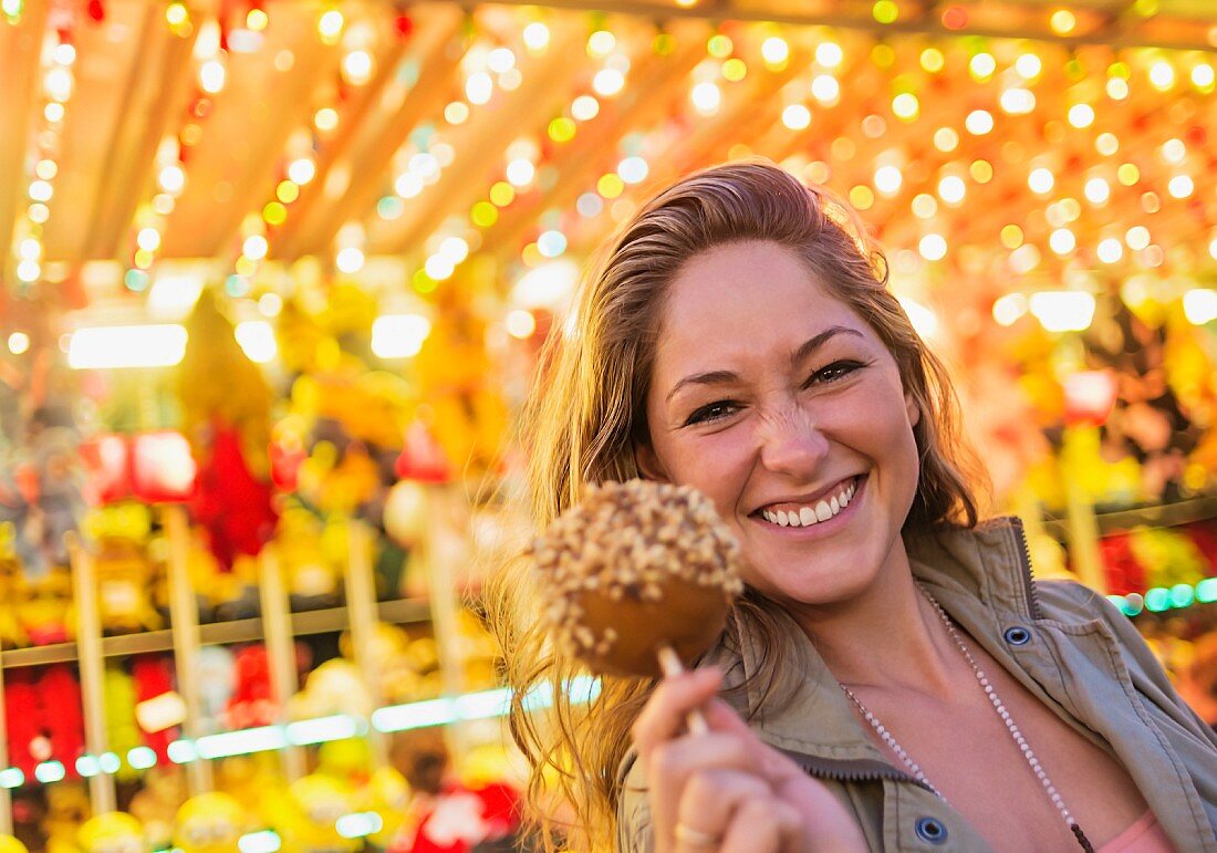 A young woman at a funfair holding a toffee apple