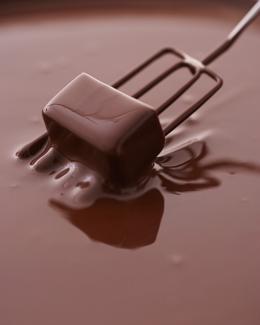 A praline being dipped into chocolate