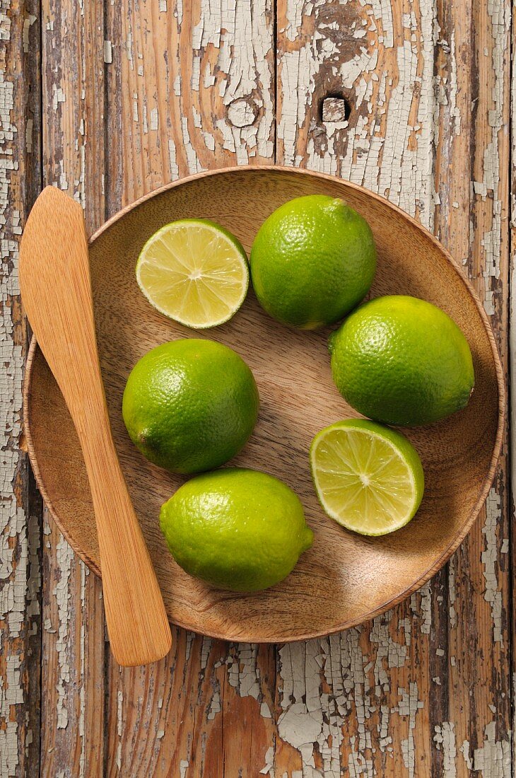 Limes, whole and halved, in a wooden bowl