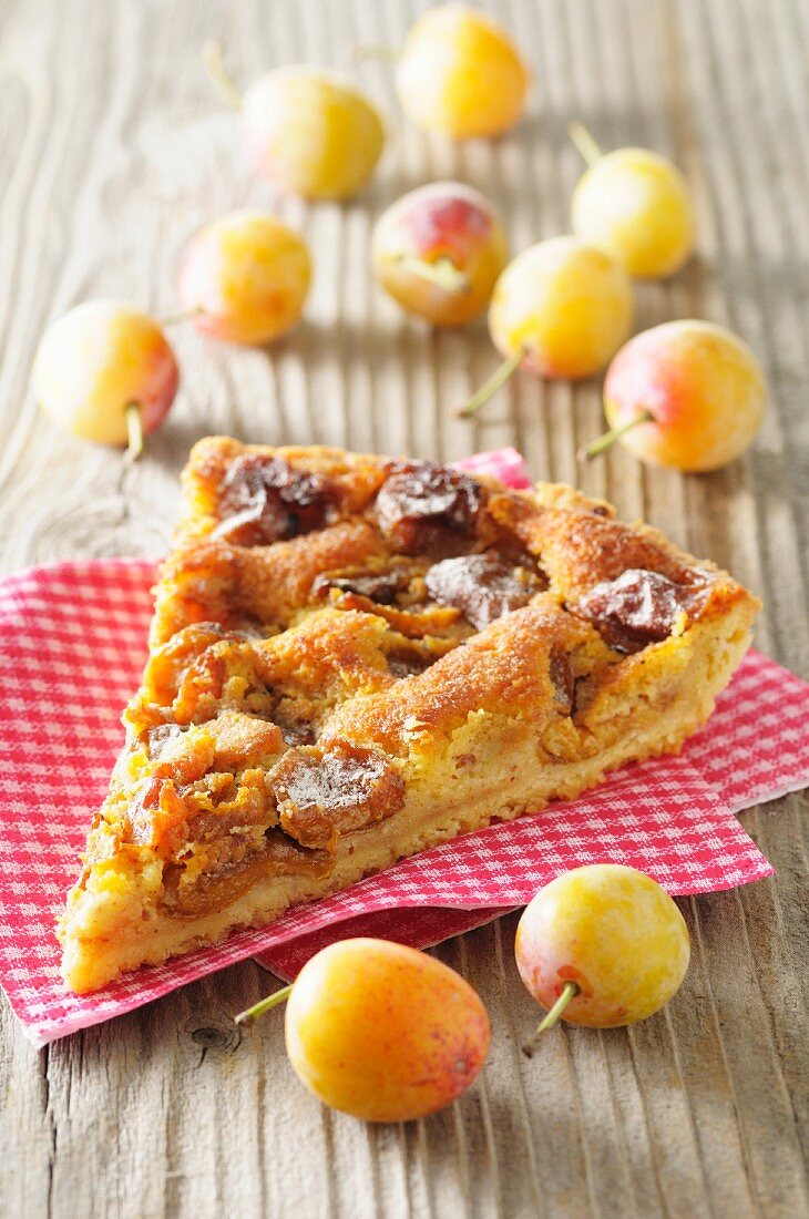 A slice of yellow plum tart on a checked napkin