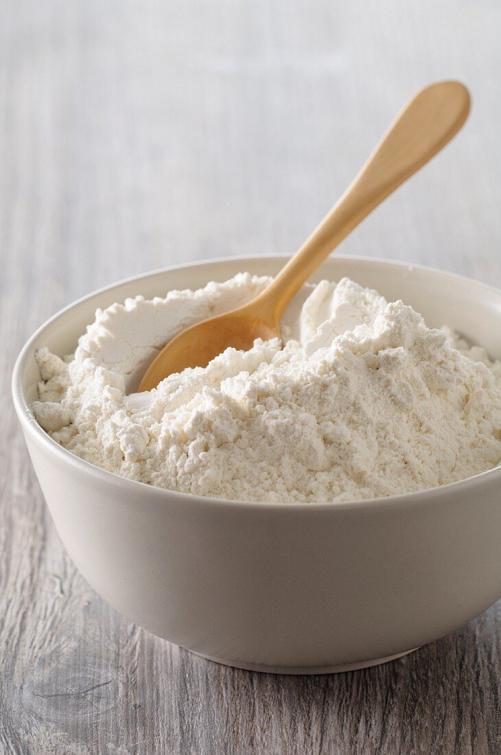 A bowl of flour with a wooden spoon