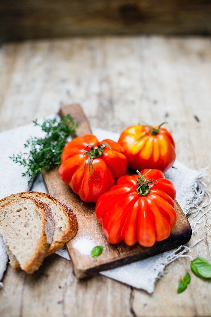 Three beefsteak tomatoes on a chopping board with salt and bread