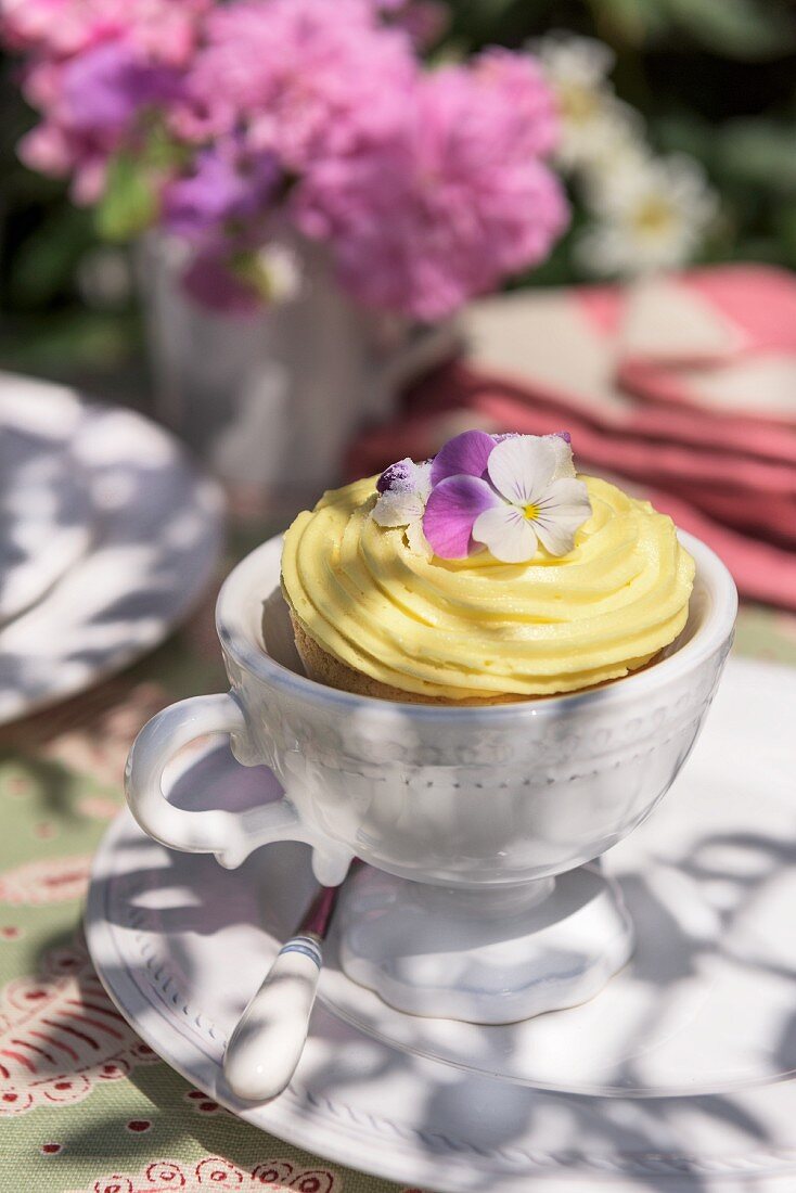 A cupcake decorated with vanilla cream and pansies on garden table