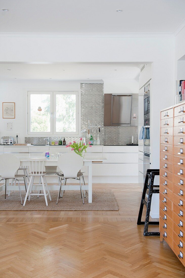 Blick von Wohnbereich mit Fischgrätparkett auf Essplatz vor moderner Küchenzeile in Weiß