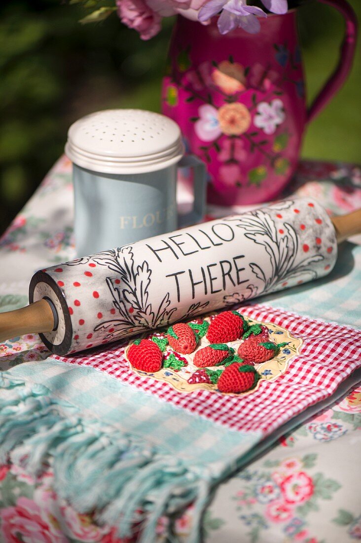 Vintage-style arrangement of rolling pin with written motto and crocheted strawberries on tablecloth on garden table
