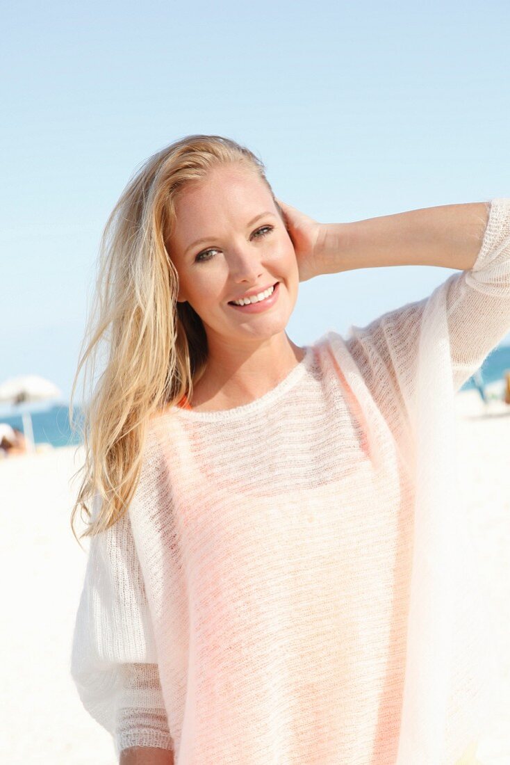 A blonde woman on the beach wearing a see-through woollen jumper