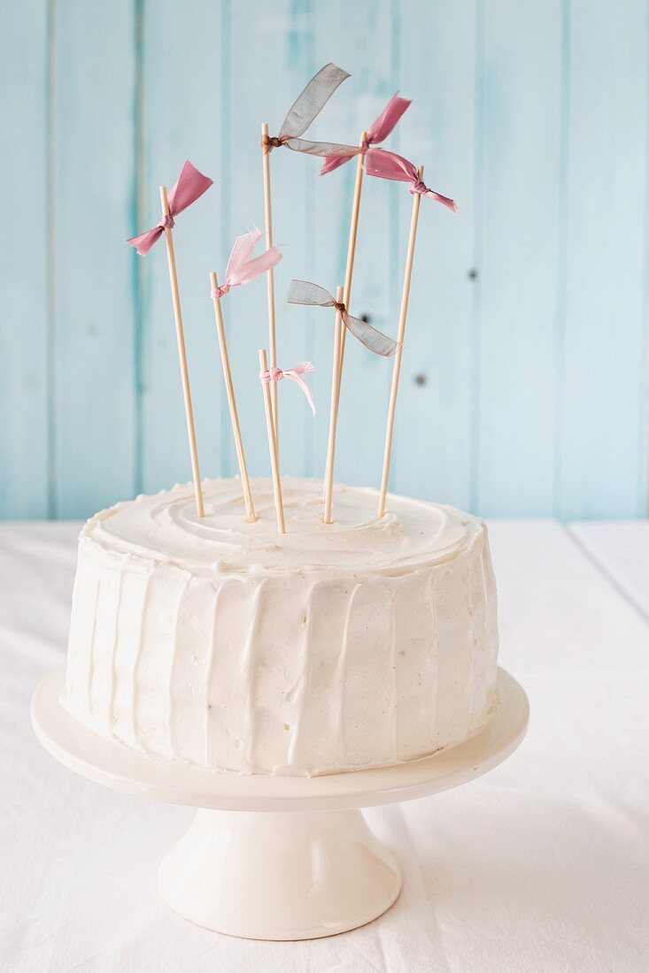 A white birthday cake with pink flags on a cake stand