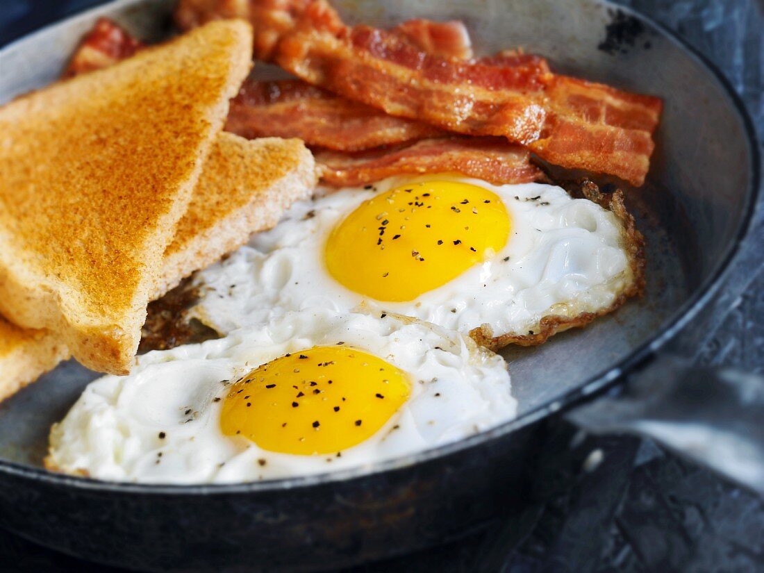 Fried eggs with bacon and toast in a pan