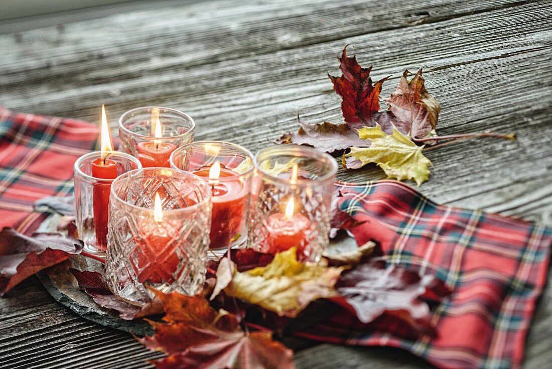 Red candles in glass lanterns and autumn leaves on tartan cloth