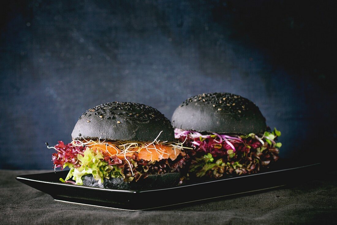 Two homemade black burgers with salmon, beetroot, sprouts and lettuce