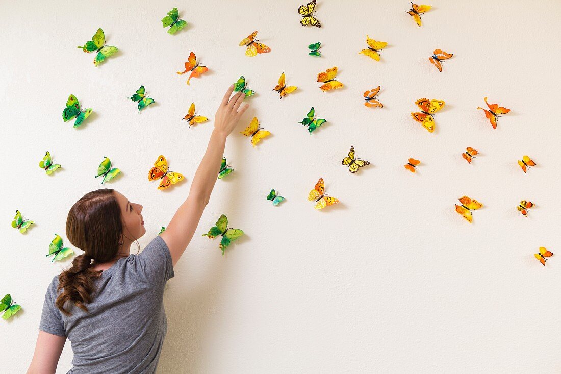 Junge Frau dekoriert Wand mit bunten Schmetterlingen