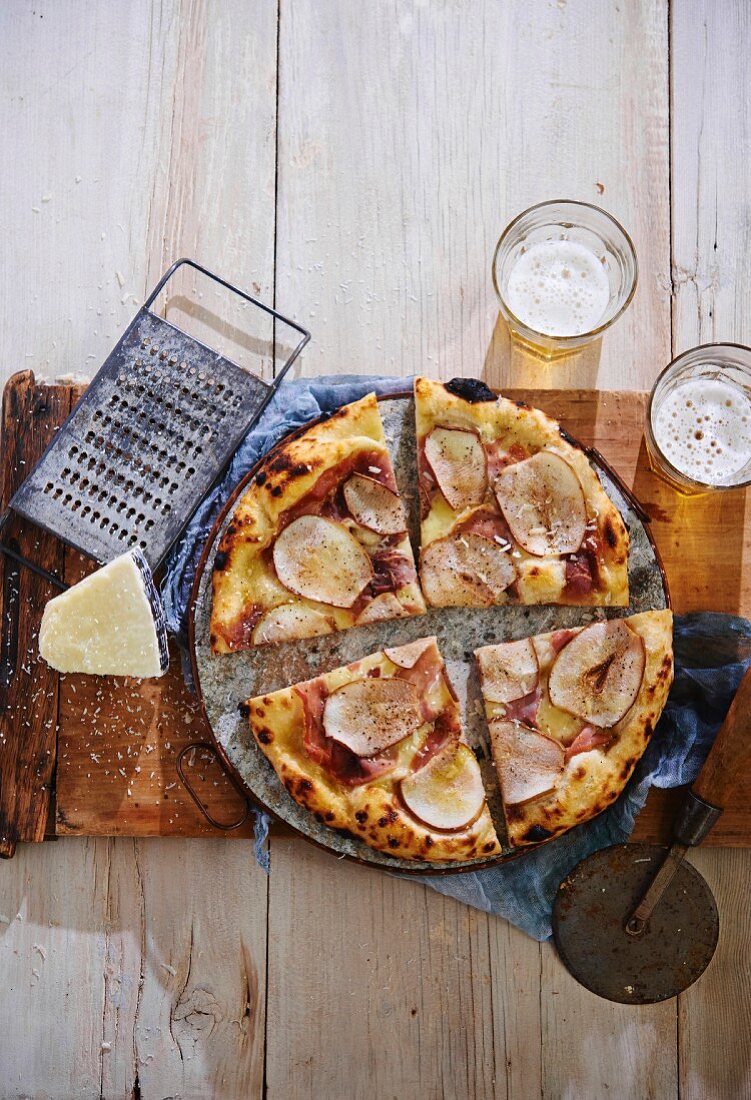 Pizza mit Schinken, Birne und Fontina-Käse auf Holzbrett (Aufsicht)