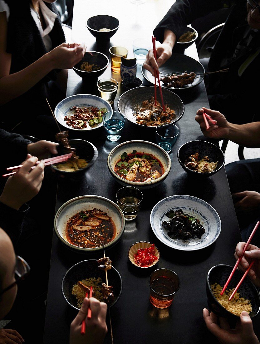 Essende Menschen an gedecktem Tisch mit verschiedenen chinesischen Gerichten
