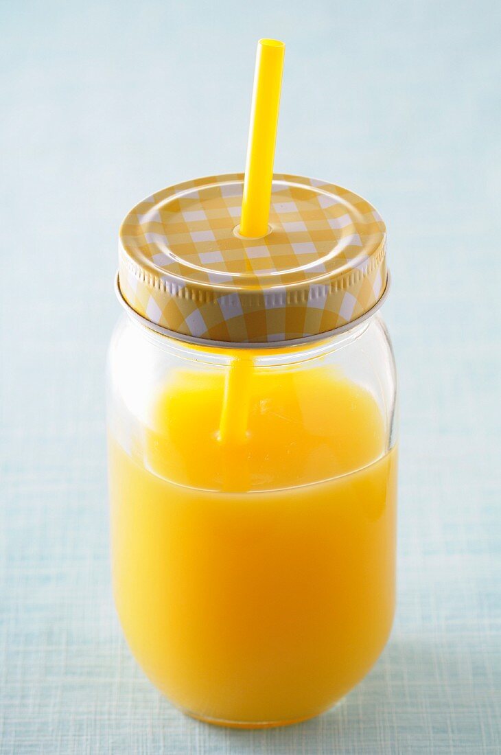 Orange juice in a screw-top jar with a straw
