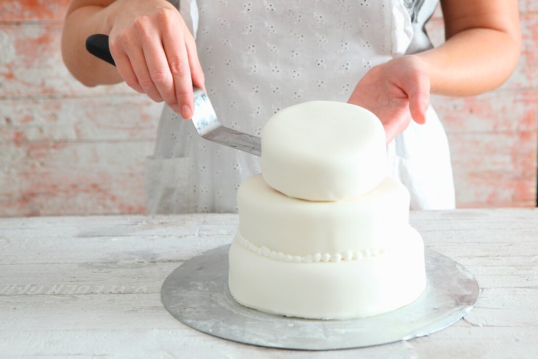 A multi-tier cake being decorated with white fondant icing